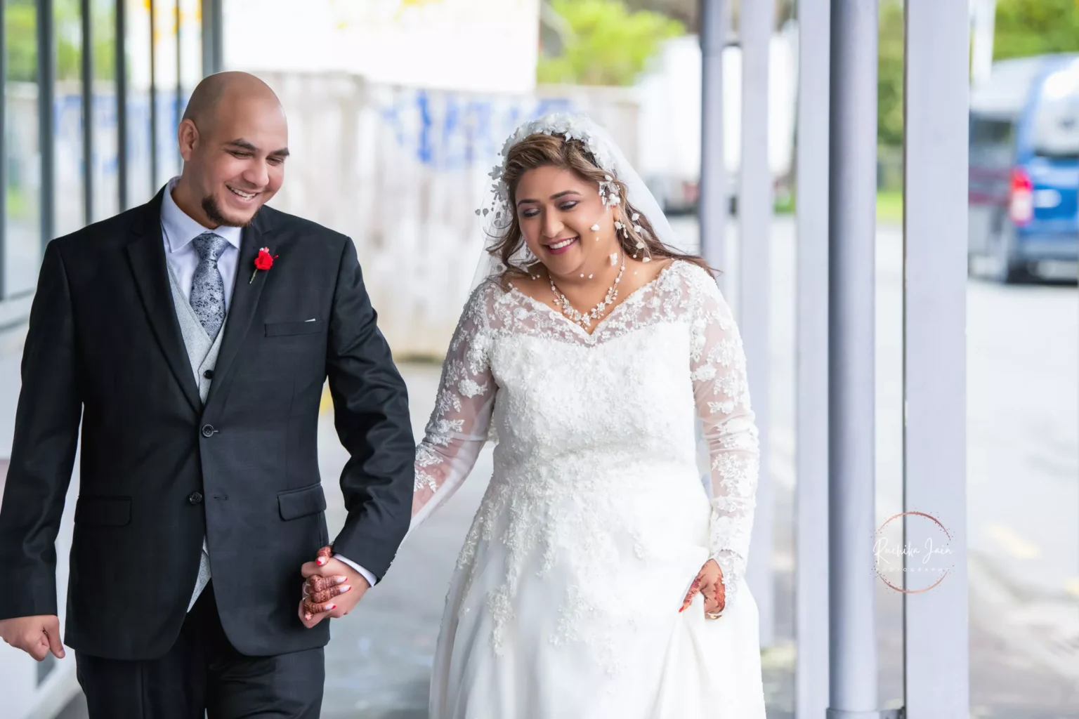 A joyful couple walking hand in hand on their wedding day in Wellington, New Zealand, with the bride wearing a beautiful lace wedding gown and the groom in a formal black suit.