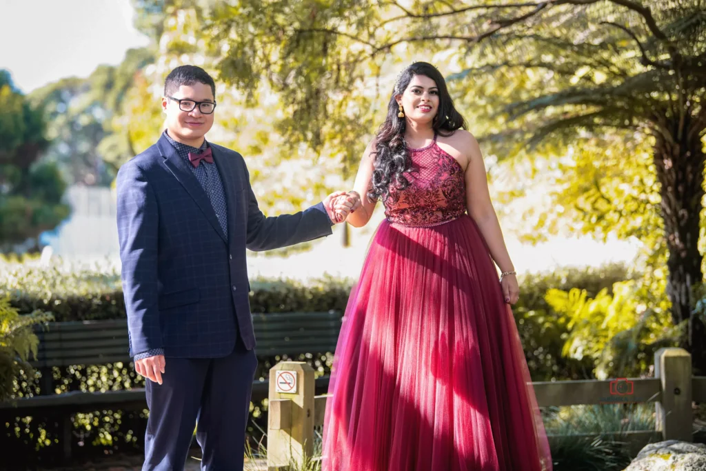 Couple holding hands outdoors, woman in a flowing red gown and man in a dark suit with a bow tie