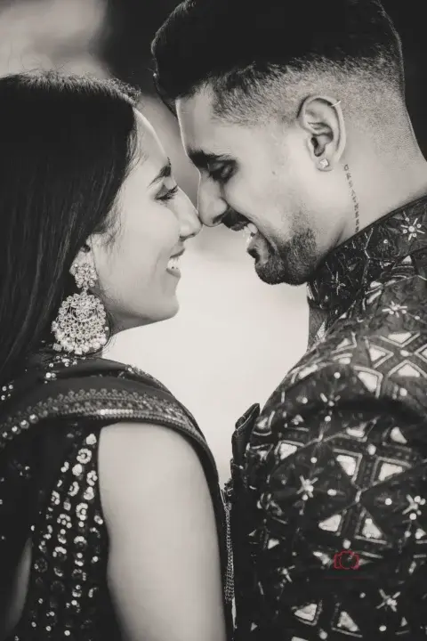 Black and white close-up of an engaged couple smiling as they lean in, foreheads touching, wearing traditional attire with intricate details