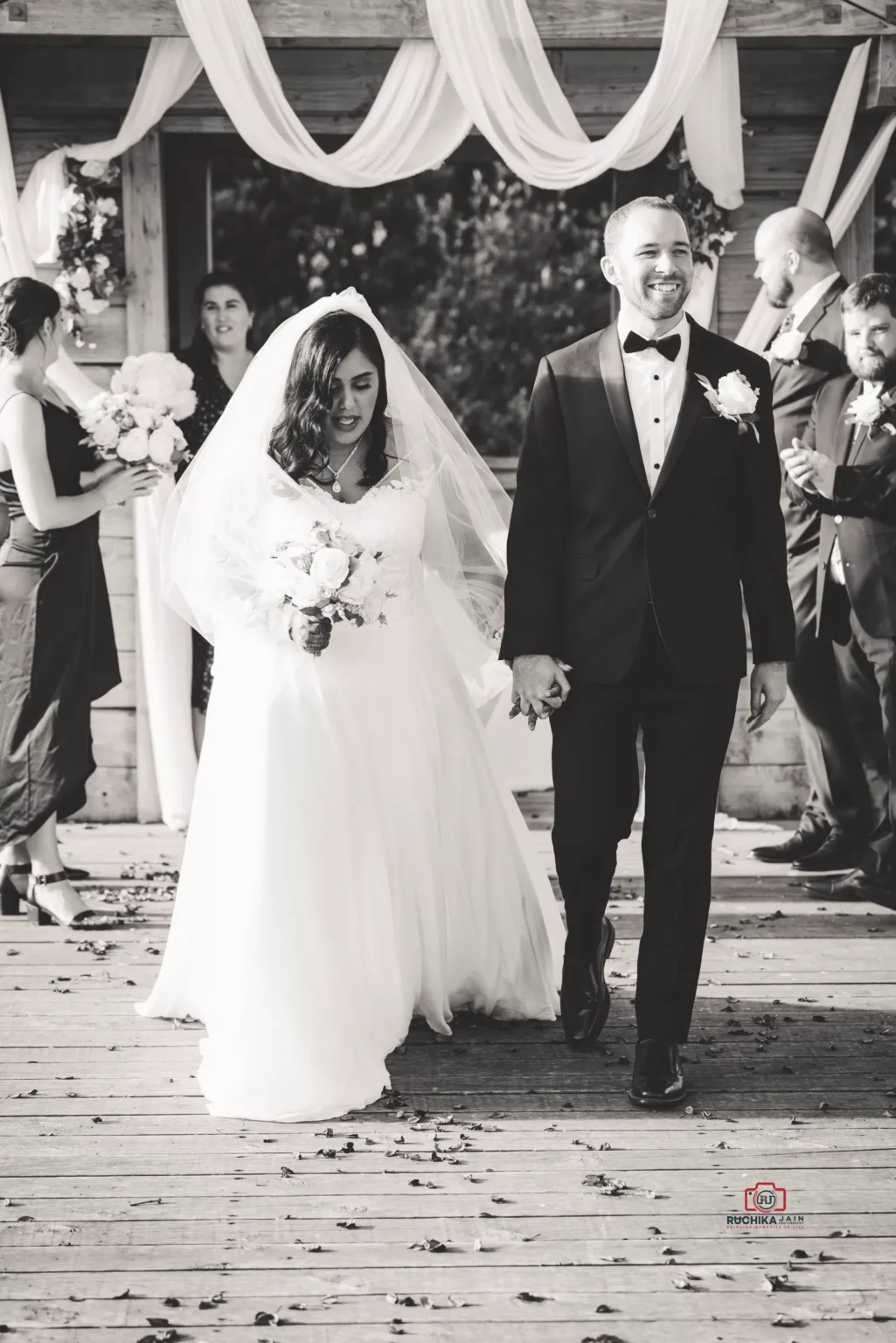 Newlywed couple walking hand in hand down the aisle, with the bride in a flowing gown and the groom in a tuxedo, smiling as guests look on