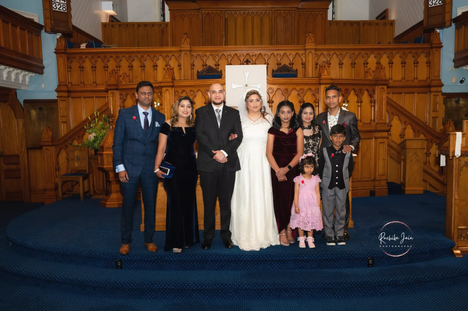 Bride and groom pose with family and friends in a church, standing in front of a wooden altar backdrop