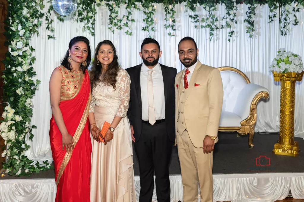 Bride and groom posing with two guests in formal attire at a wedding reception, surrounded by floral and gold decor