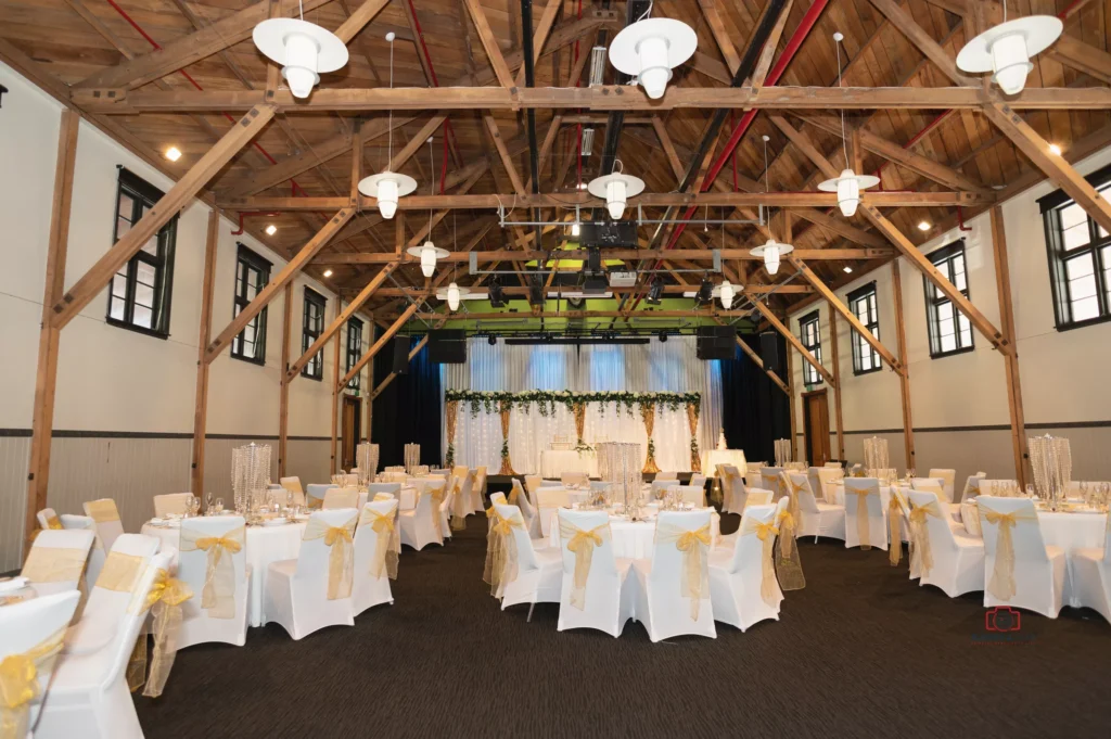 Elegant wedding reception setup at Silver Stream Retreat in Upper Hutt, featuring wooden beams, white and gold decor, and a beautifully lit stage with greenery