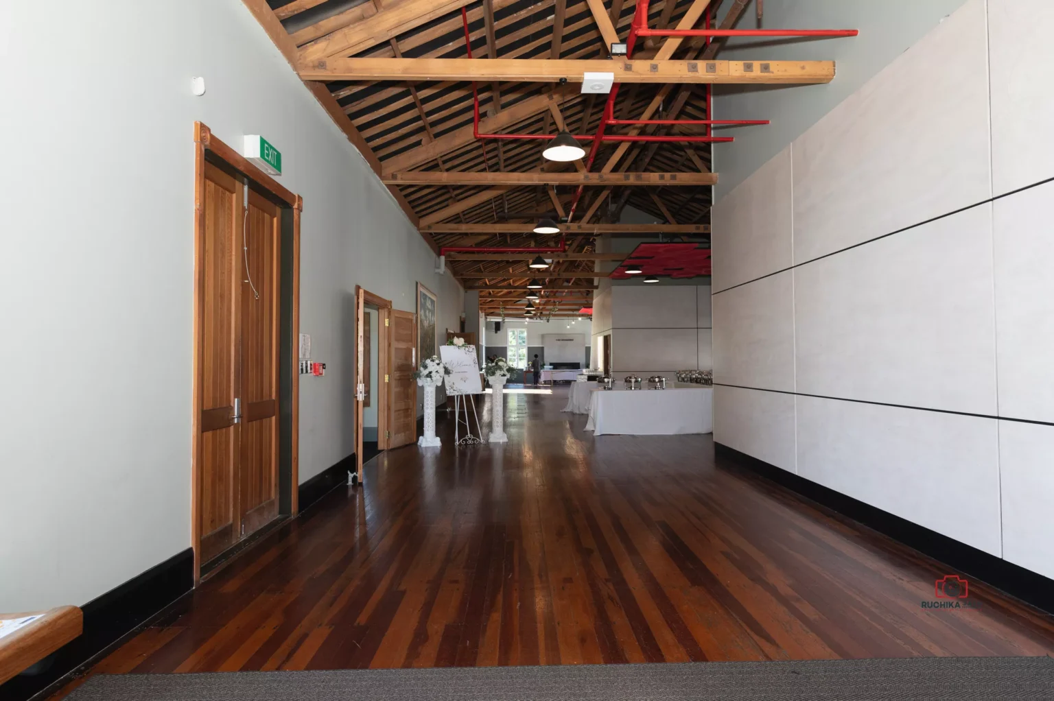 Spacious hallway in a wedding venue featuring polished wooden floors, high ceilings with exposed beams, and modern decor setup