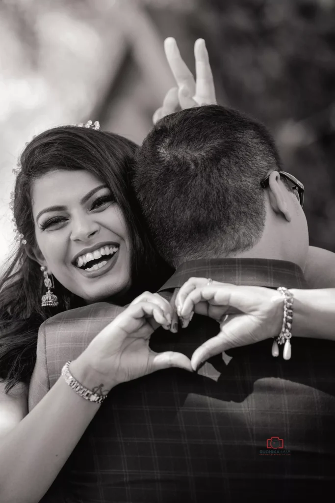 Woman smiling and making a heart shape with her hands behind a man's back, playfully posing with bunny ears gesture