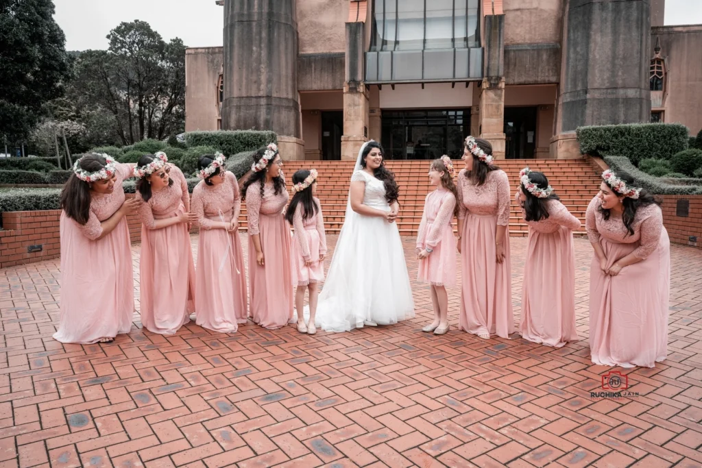 Bride standing with bridesmaids in pink dresses and flower crowns outside a large building