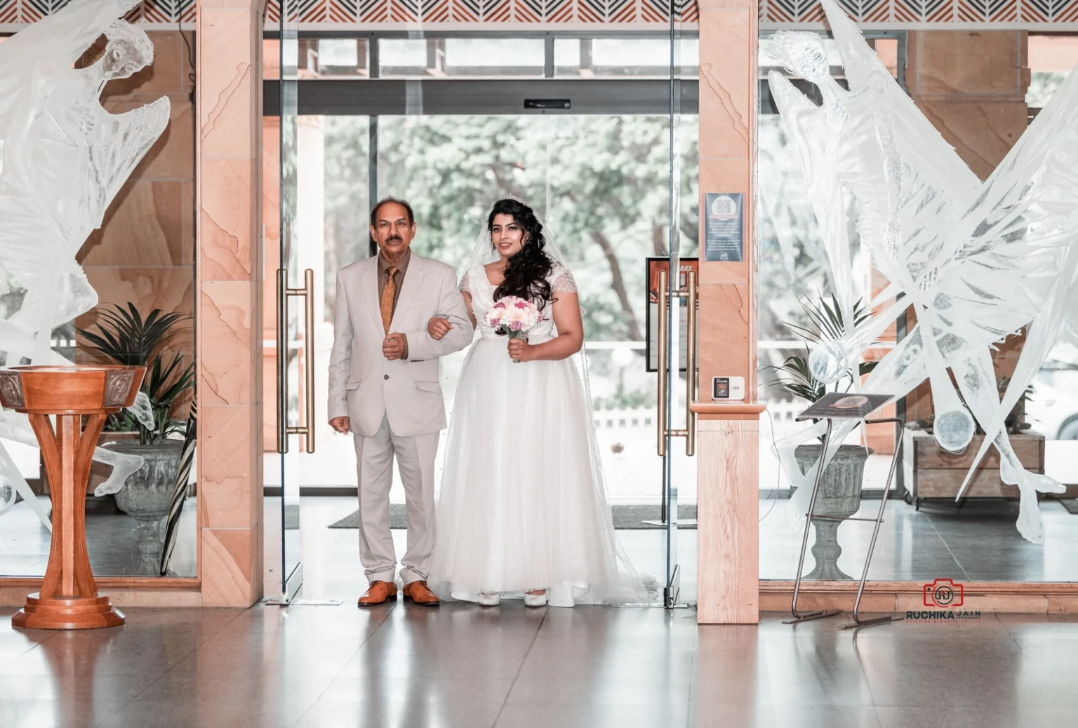 Bride in white gown walking arm-in-arm with her father at the entrance of the venue.