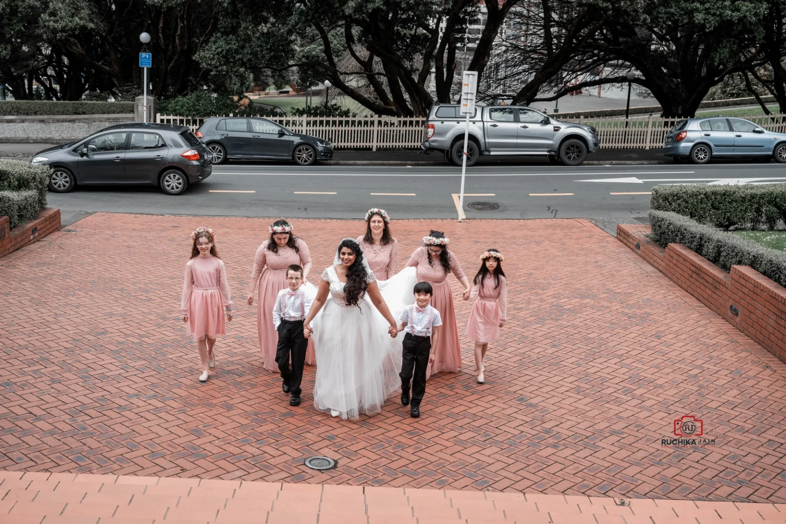 Bride walks with flower girls and ring bearers in coordinated outfits outside wedding venue