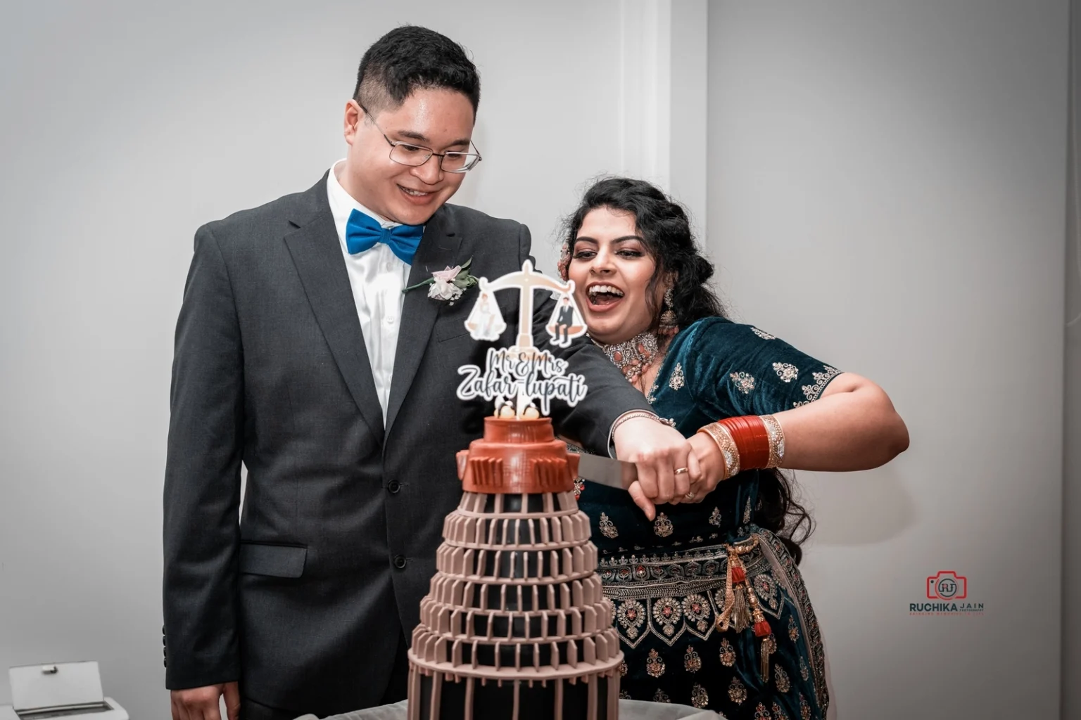 Bride and groom cutting a multi-tiered wedding cake decorated with a custom topper reading "Mr & Mrs Zabar Lupati"