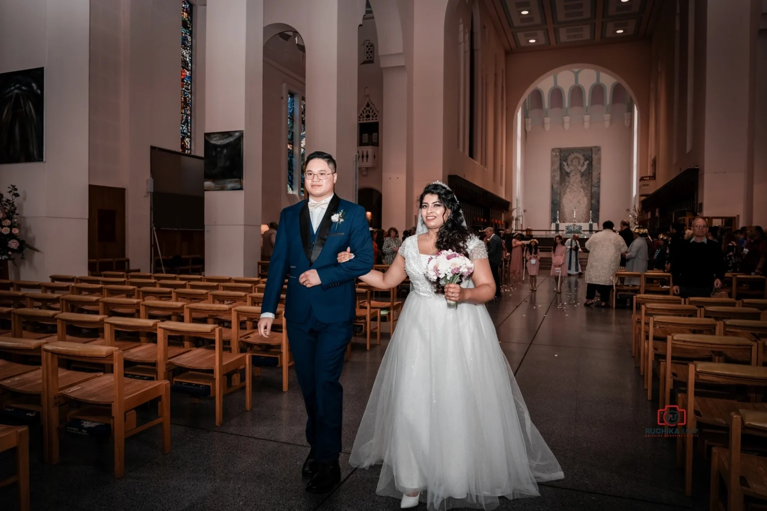 Bride and groom walk arm in arm down the church aisle, smiling as they exit the wedding ceremony