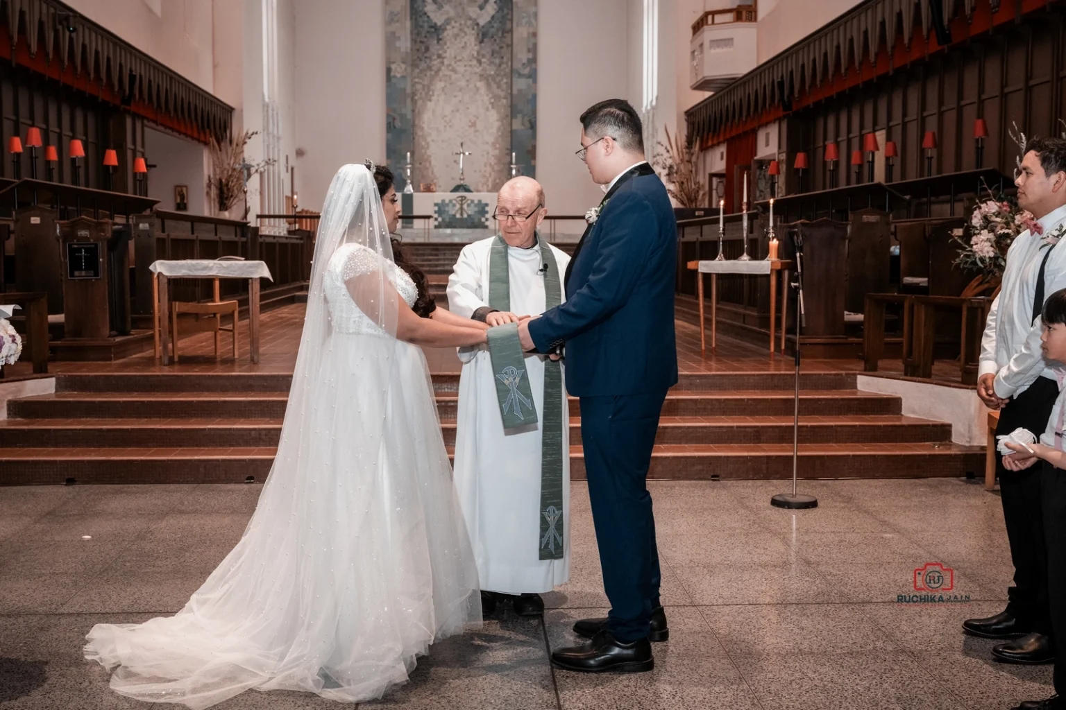 Bride and groom holding hands during wedding vows at a church altar with the officiant present