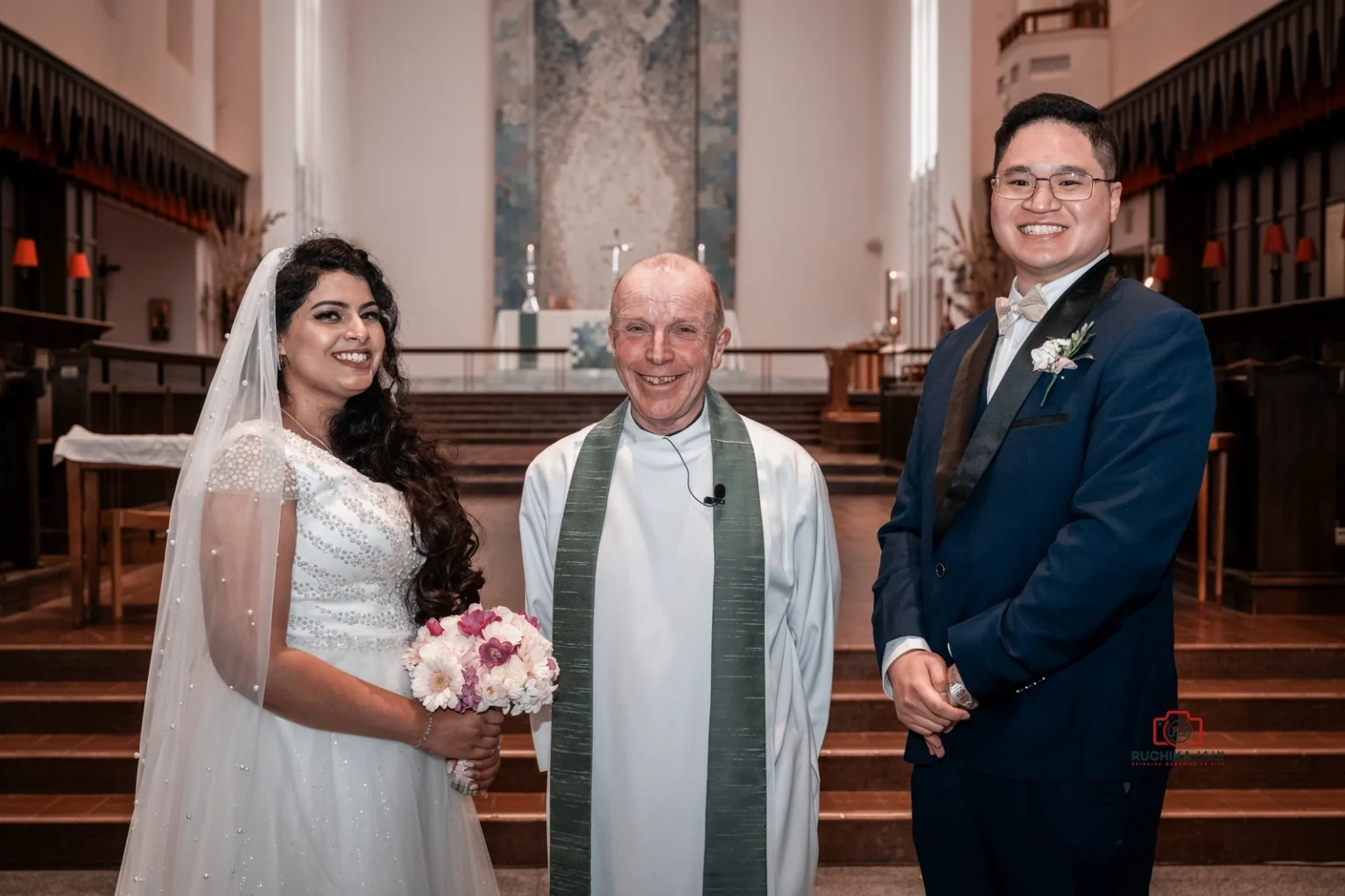 Bride and groom smiling with officiant inside a church after wedding ceremony