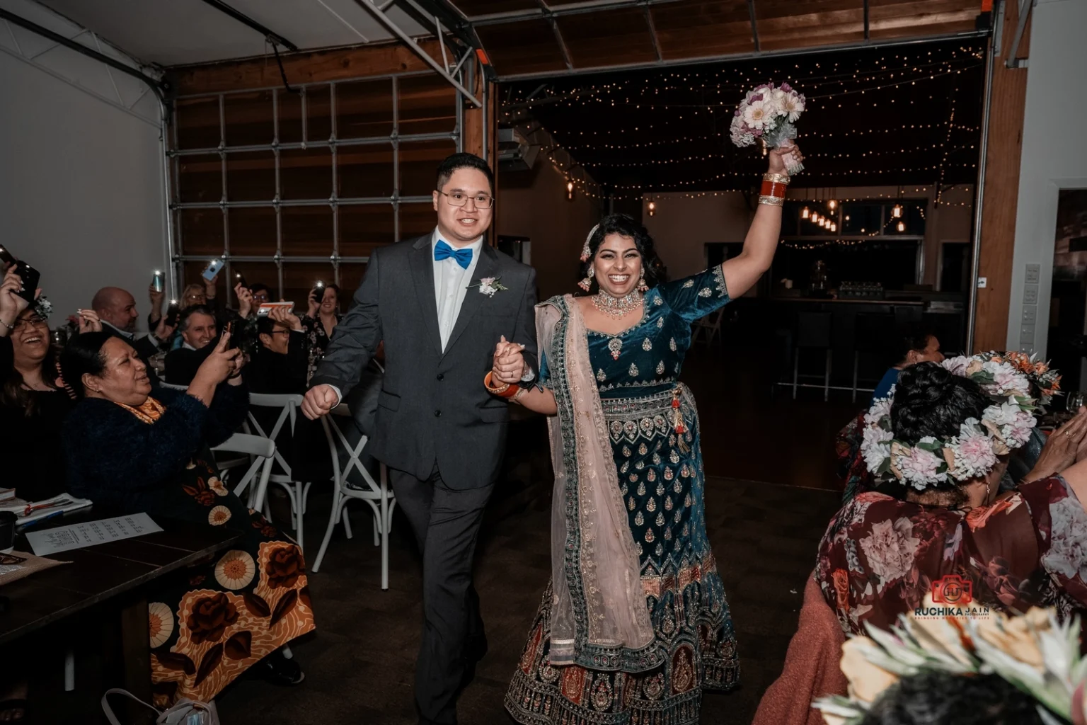 ride and groom making an enthusiastic entrance into the wedding reception, holding hands and smiling as guests cheer and take photos