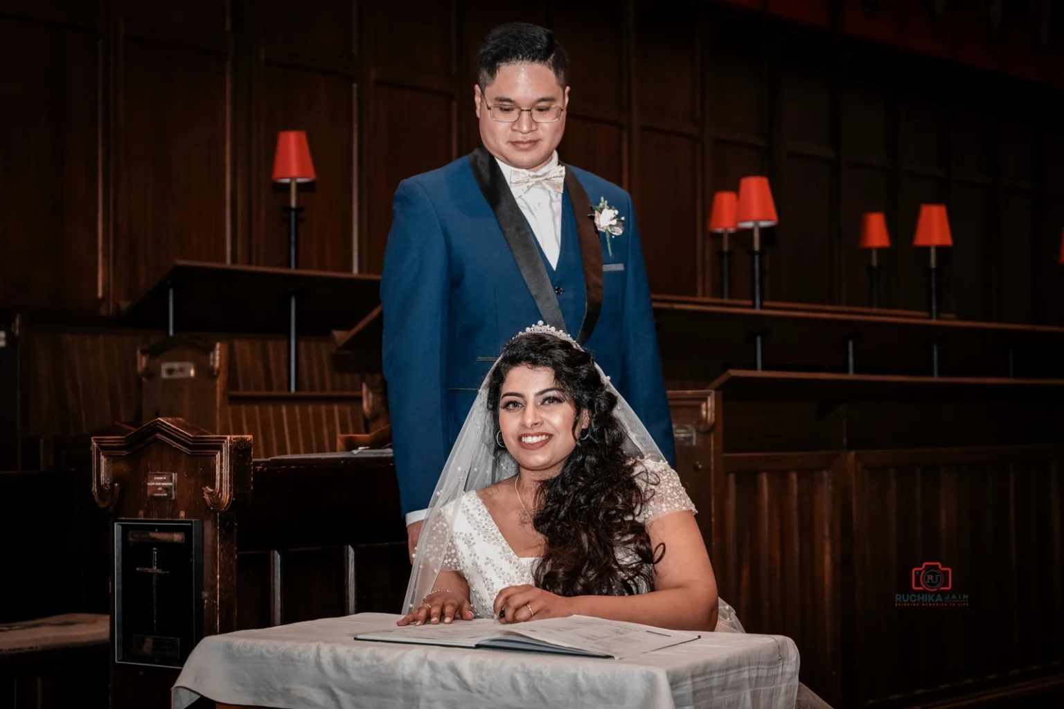 Smiling bride seated while signing the marriage certificate with groom standing beside her