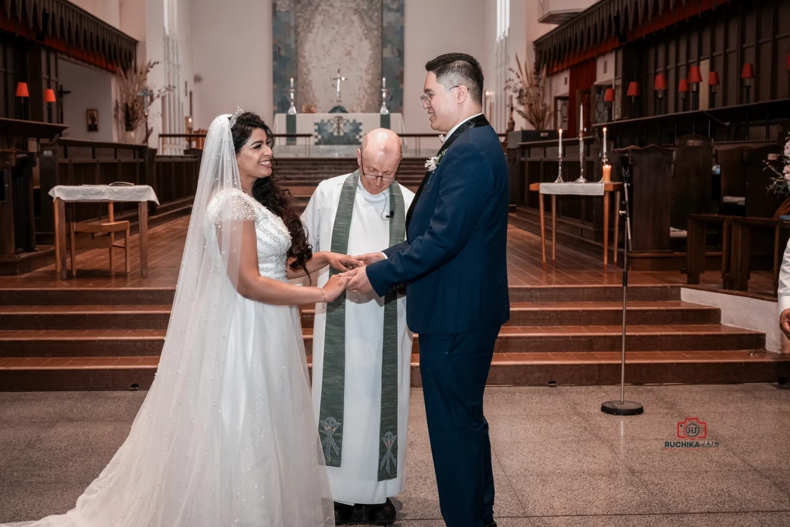 Bride and groom smiling and holding hands at church altar with officiant in background