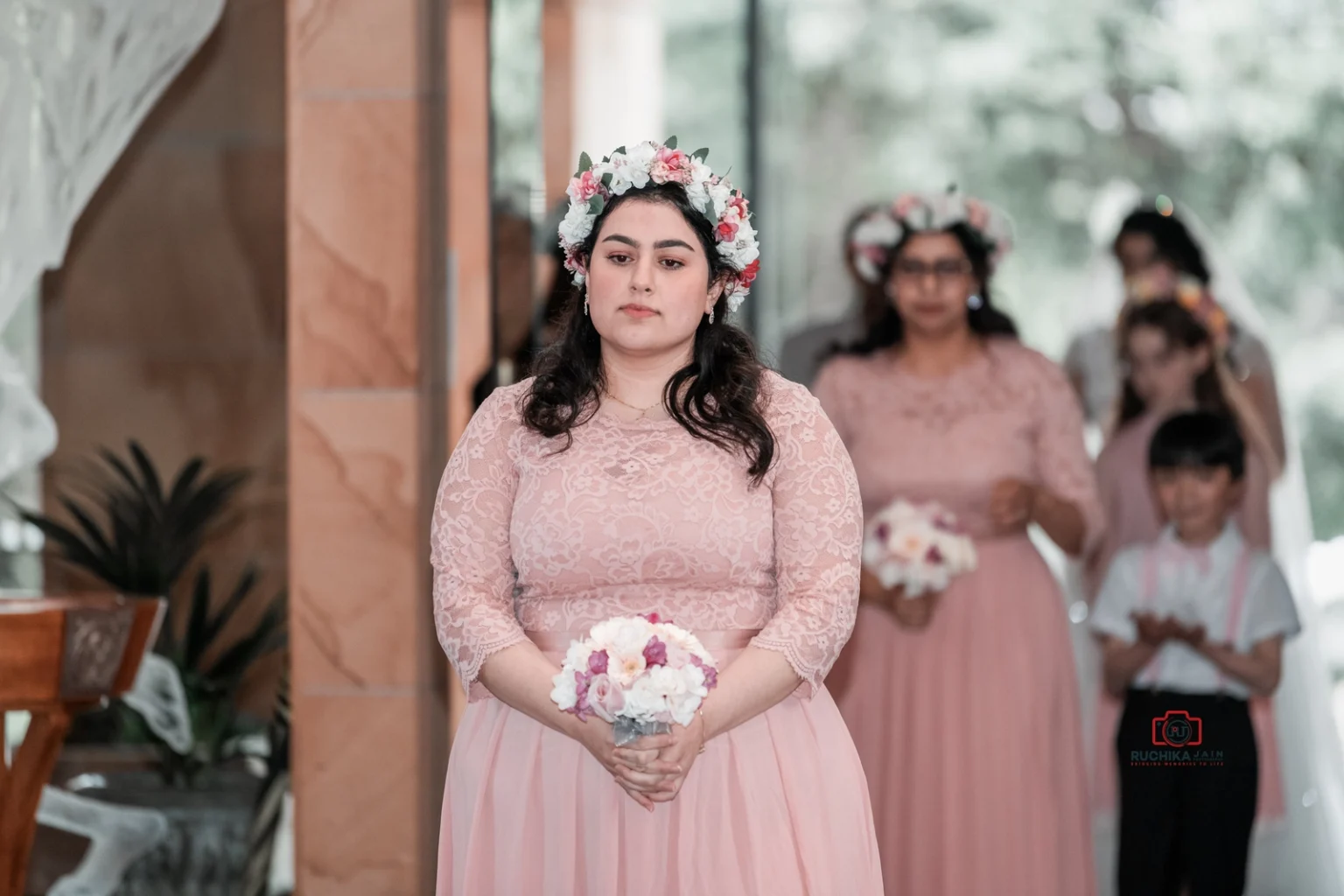 Bridesmaid in pink dress and floral crown holding a bouquet, entering the church for the ceremony.