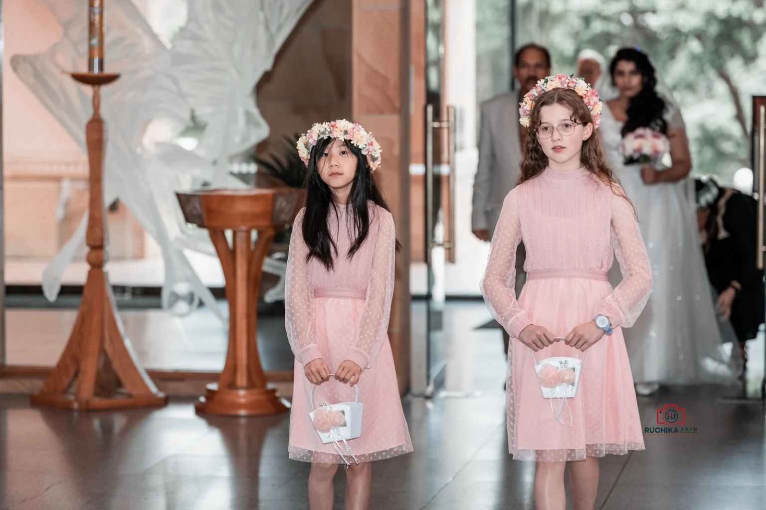 Two flower girls in pink dresses and floral crowns holding baskets as they enter the church.