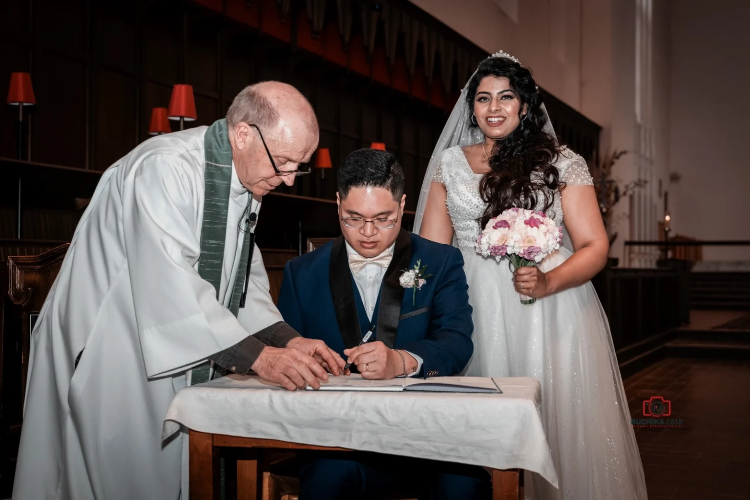 Groom signing marriage certificate, with bride and priest by his side