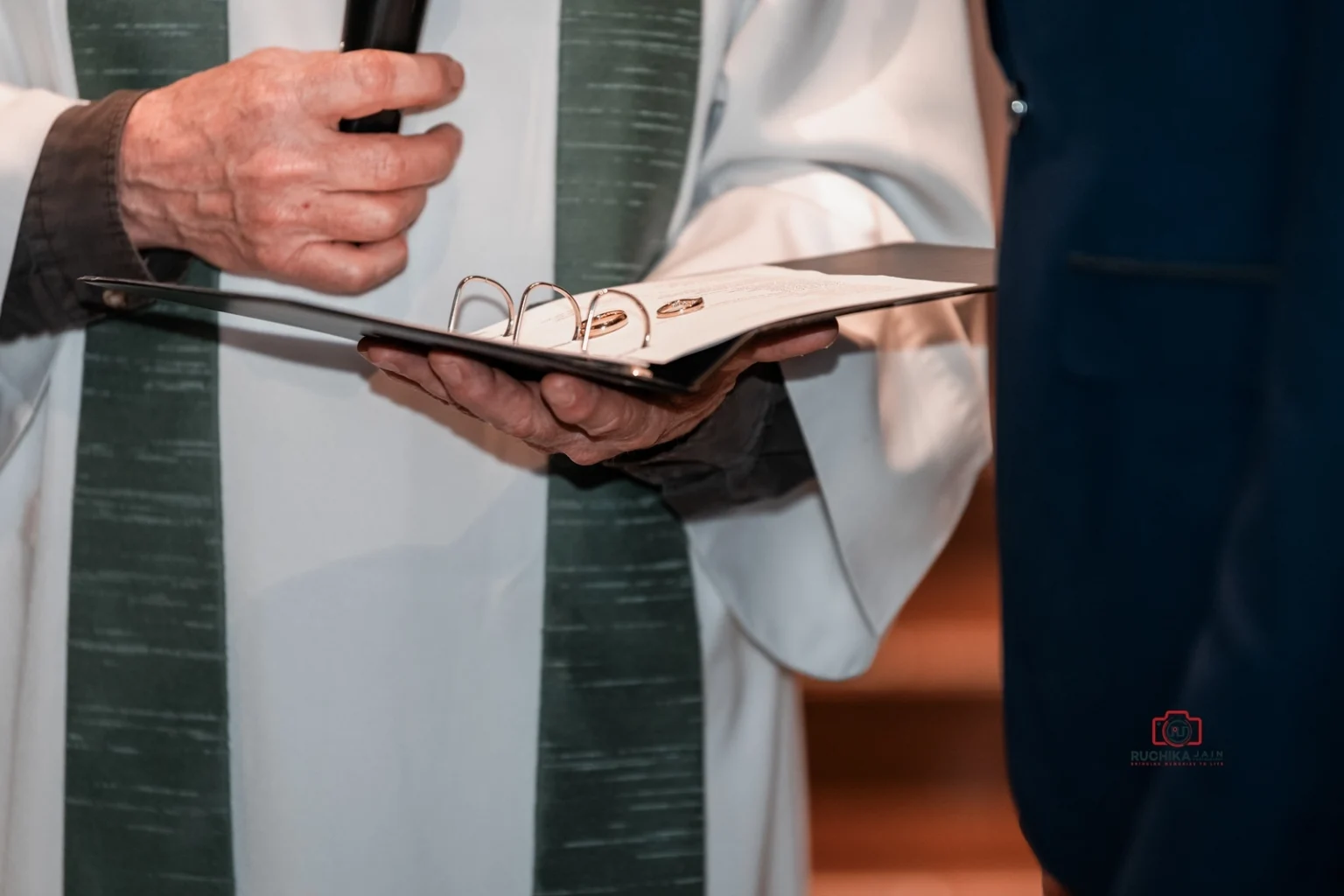 Close-up of officiant’s hands holding a black binder with wedding vows