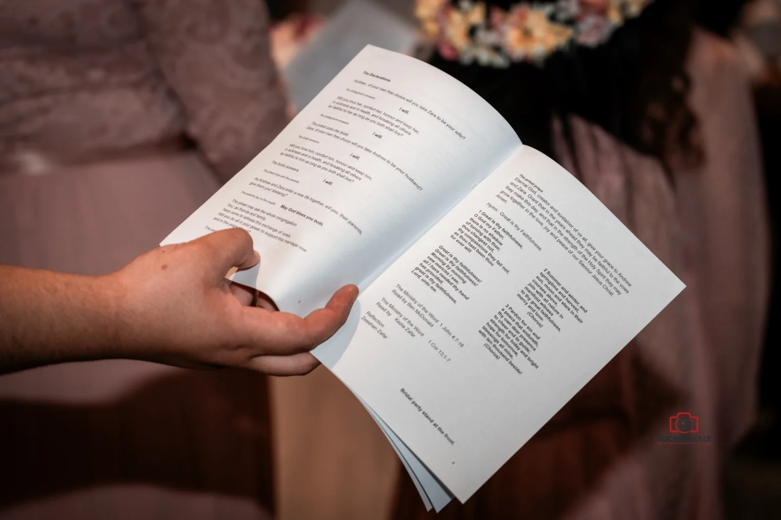 Close-up of a hand holding a wedding ceremony program booklet, displaying vows and prayers