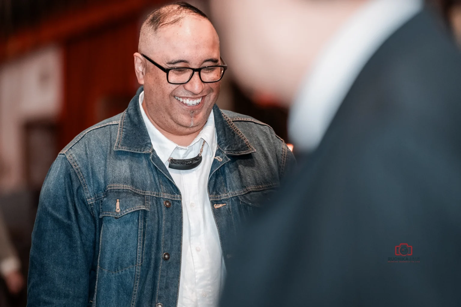 Smiling wedding guest wearing glasses and a denim jacket during the ceremony