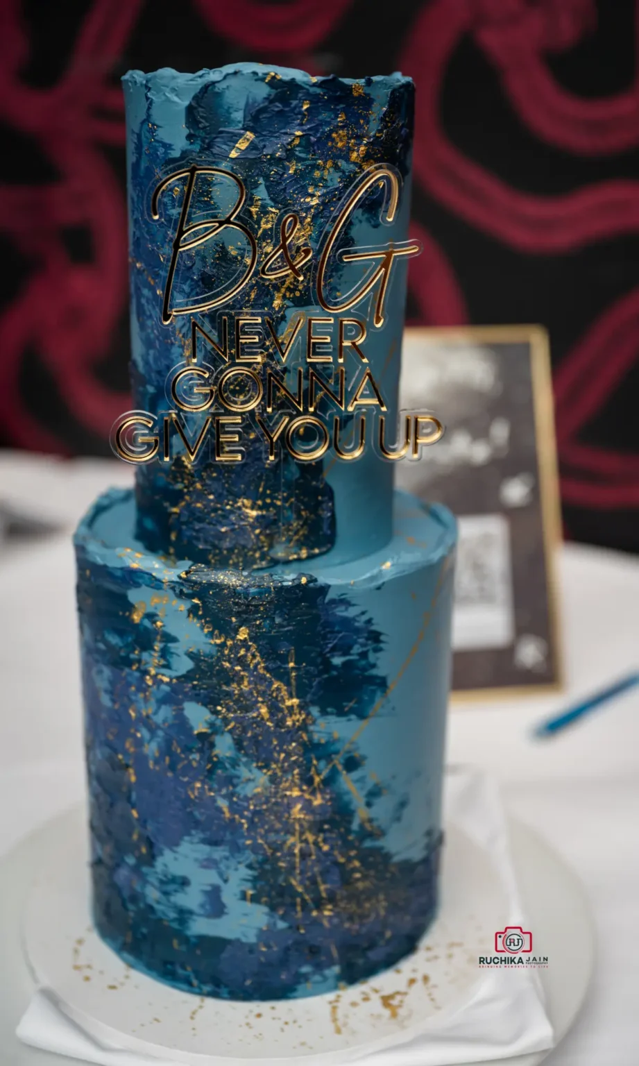 Blue and gold wedding cake with custom topper reading 'B & G Never Gonna Give You Up