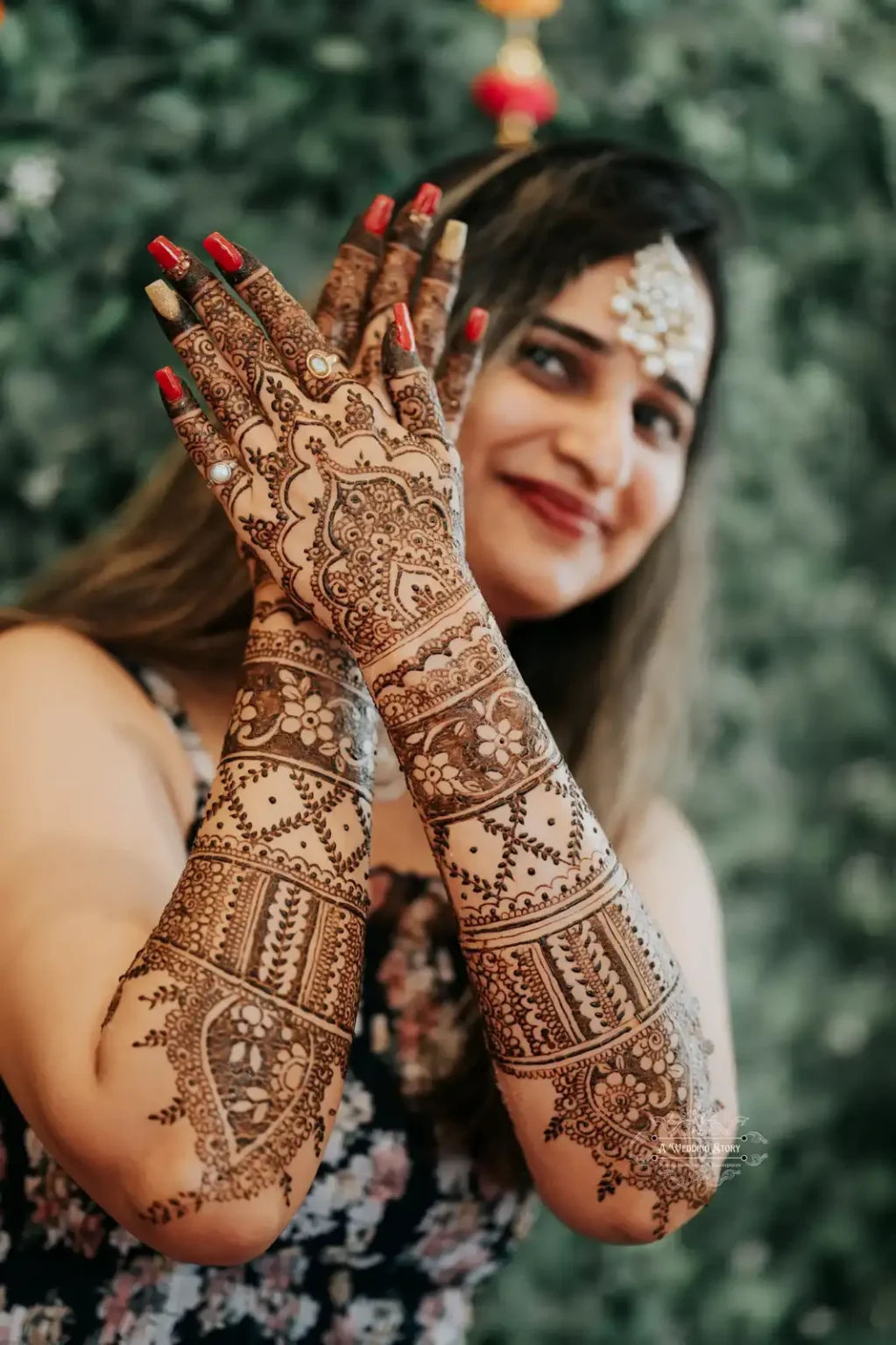 Close-up of a bride showcasing her elegant mehndi art with intricate details, complemented by a green floral backdrop, captured during a Mehndi ceremony in Wellington