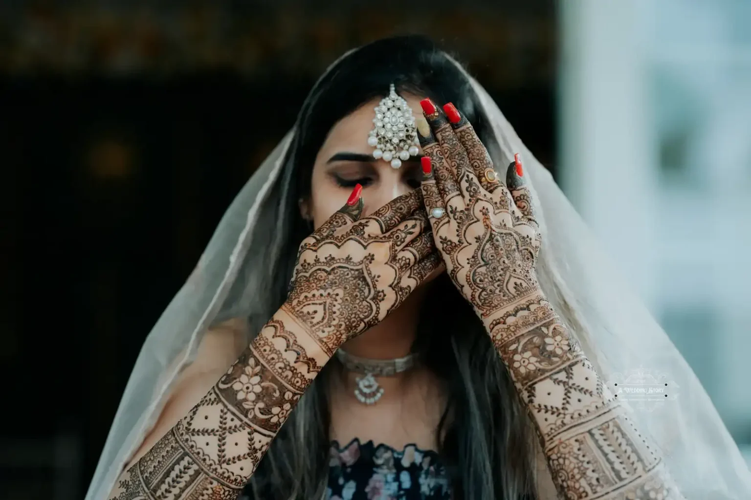 Indian bride covering her face with hands adorned in intricate mehndi designs, wearing traditional jewelry and a veil, captured in Wellington by A Wedding Story