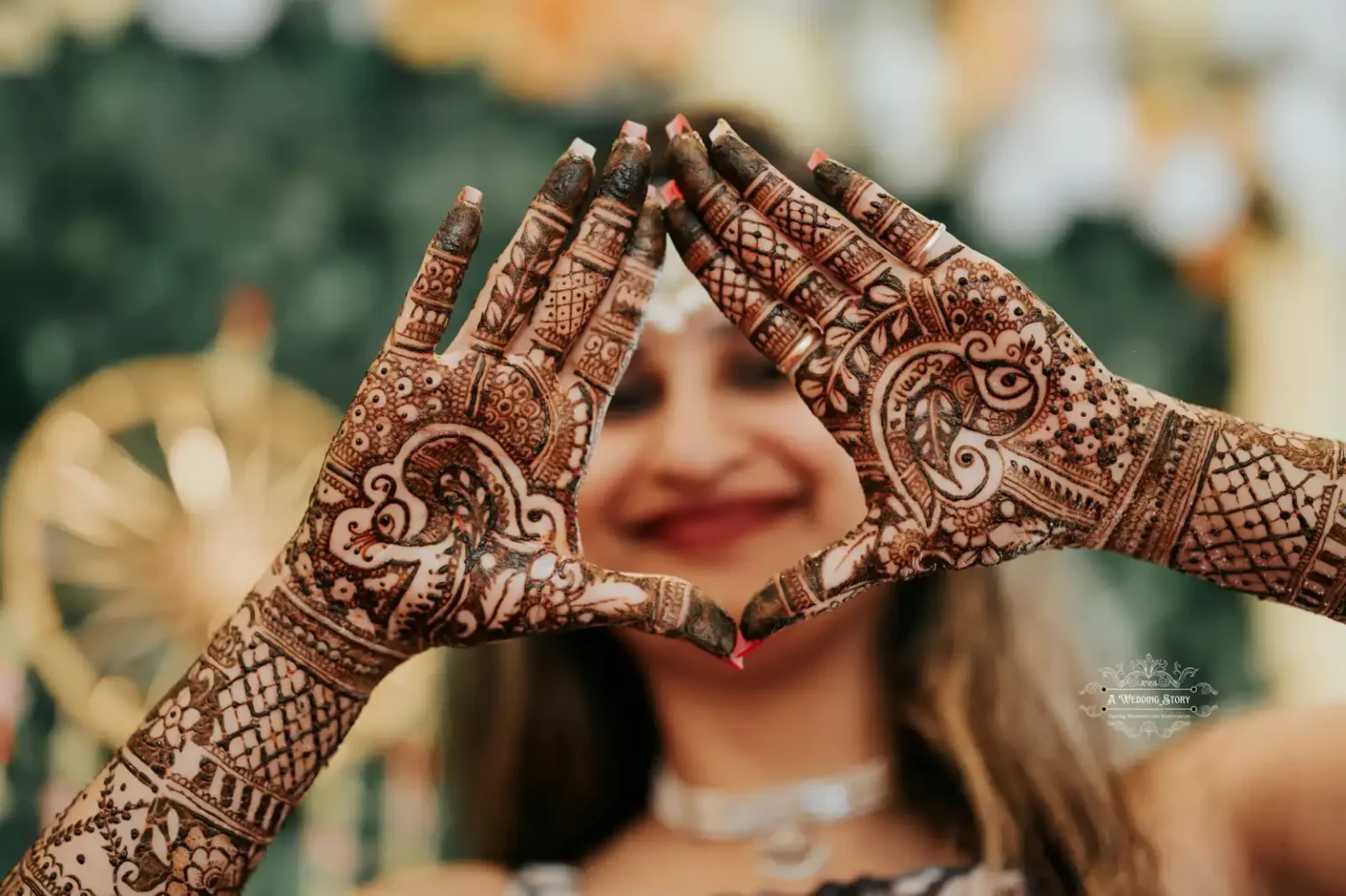 Indian bride forming a heart shape with her hands adorned with intricate mehndi designs, smiling in the background, captured during a pre-wedding ceremony in Wellington by A Wedding Story