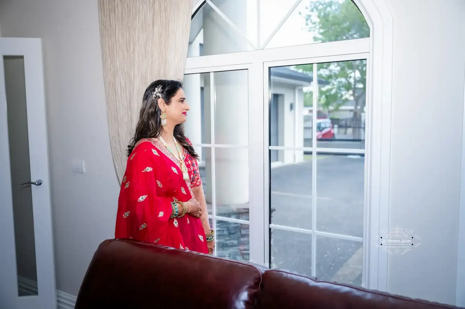 Bride in traditional red attire looking out the window, captured by Wedding Photography in Wellington