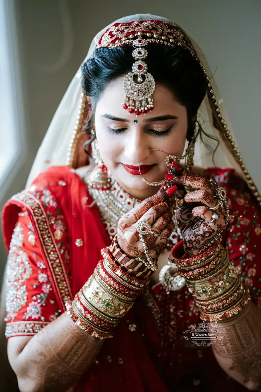 Bride in traditional red attire and intricate jewelry, holding her nose ring with eyes closed, capturing a serene moment.