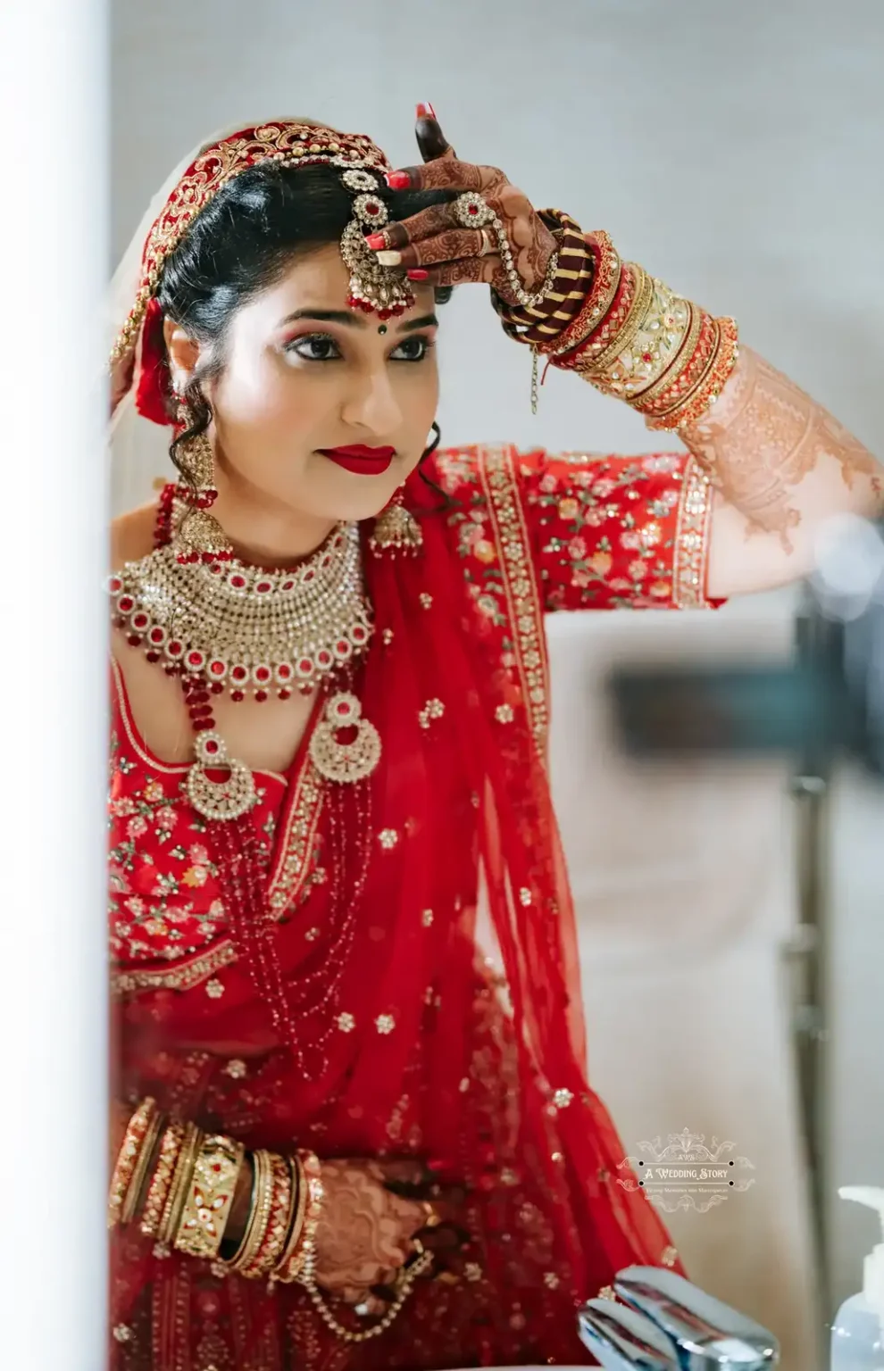 Bride in traditional red attire, adjusting her headpiece with henna-decorated hands, preparing for her wedding ceremony.