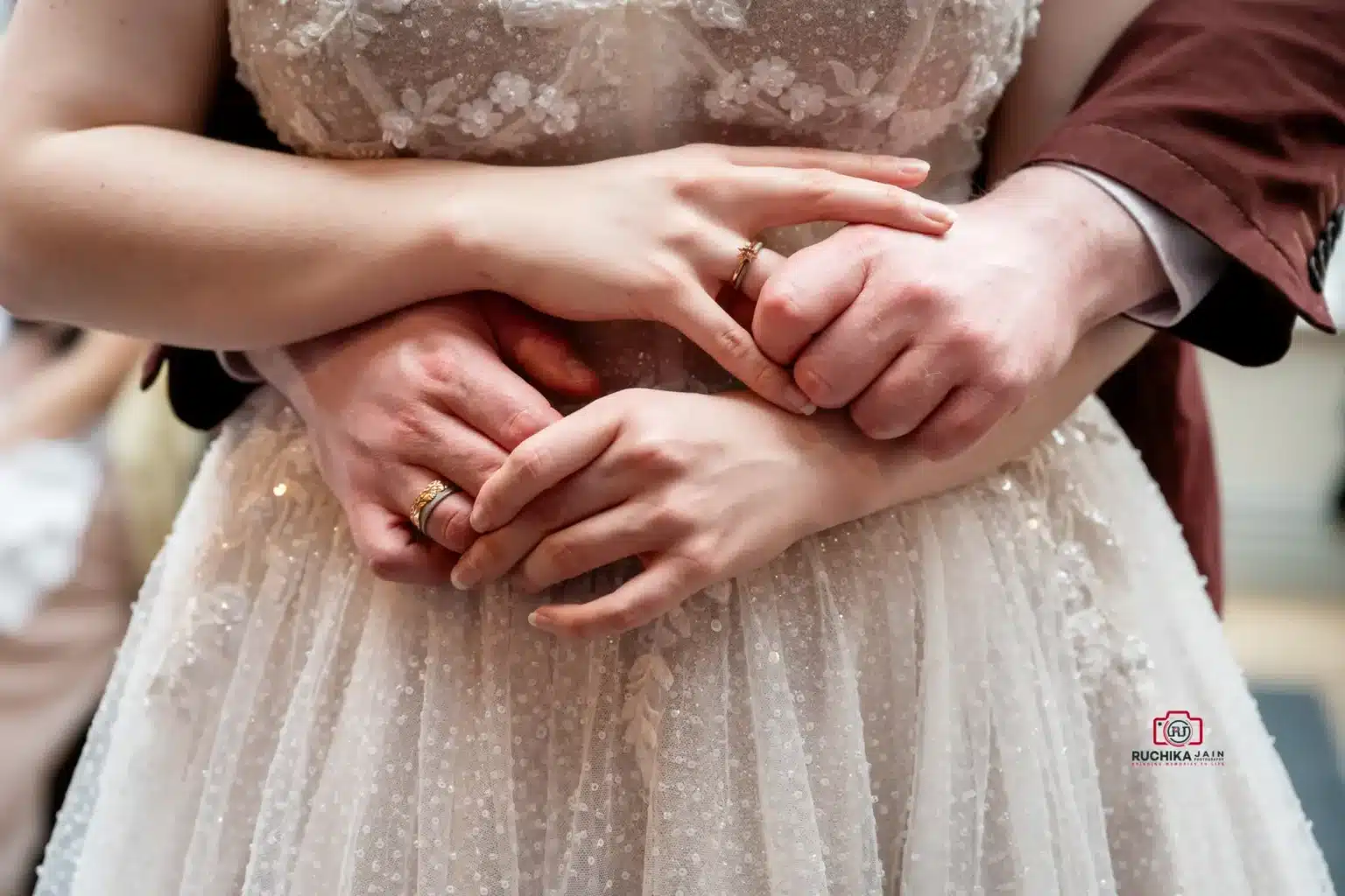 Close-up of the bride and groom’s hands intertwined, showing wedding rings against the bride's beaded dress