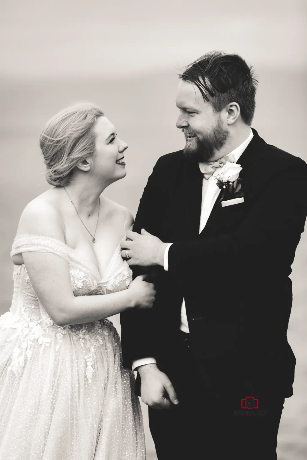 Black and white photo of a bride and groom smiling at each other on their wedding day.