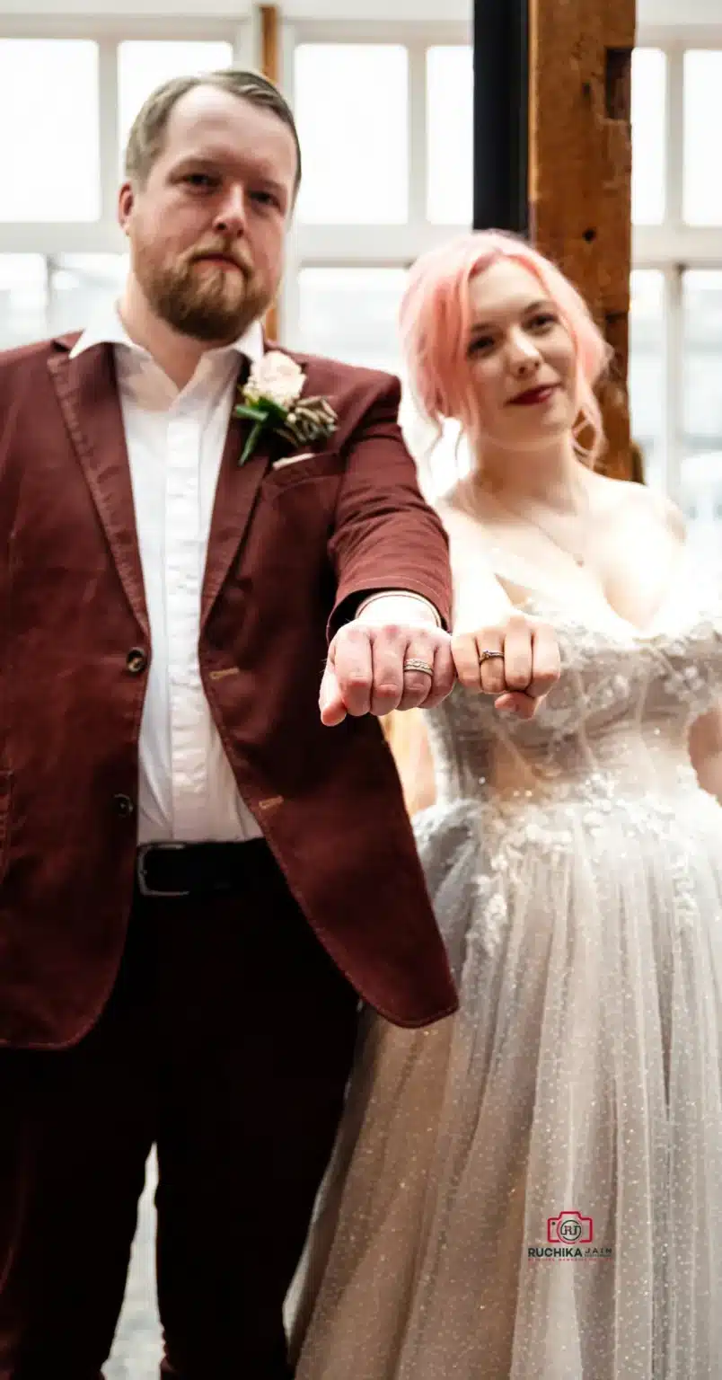 Bride and groom proudly display their wedding rings with fists extended, showcasing their commitment on their special day