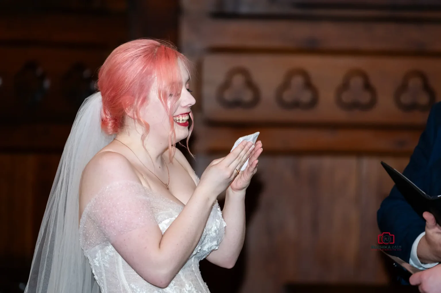 Bride with pink hair smiling and holding her written vows during a wedding ceremony in a church.