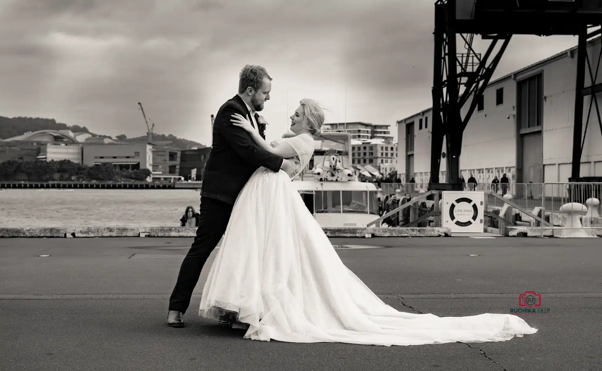 Black and white photo of a bride and groom dancing outdoors, with the groom dipping the bride as they smile at each other