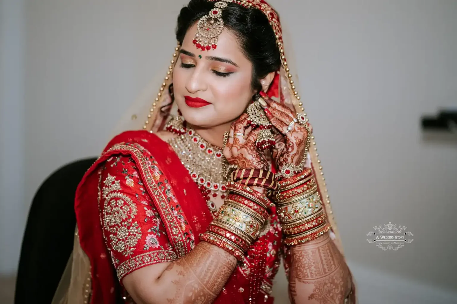 Beautiful bride in red traditional attire, adjusting earrings with intricate henna on hands, preparing for her wedding ceremony.