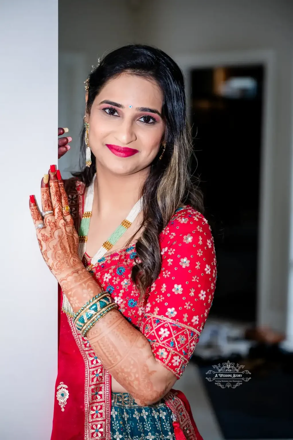 Bride in traditional red dress with intricate henna on her hands, smiling and posing gracefully.