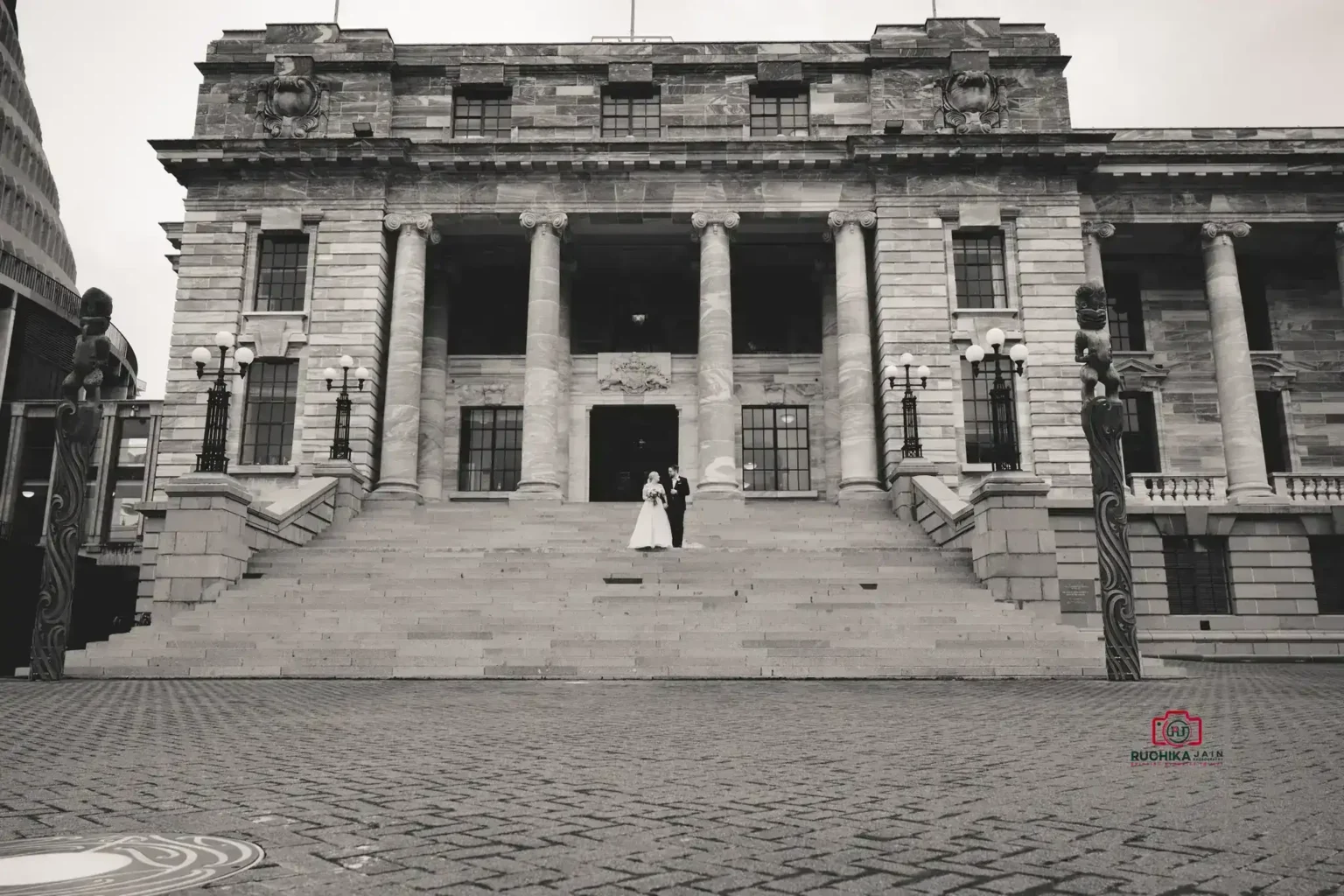 Bride and groom stand on the grand stone steps of a historic building with large columns.