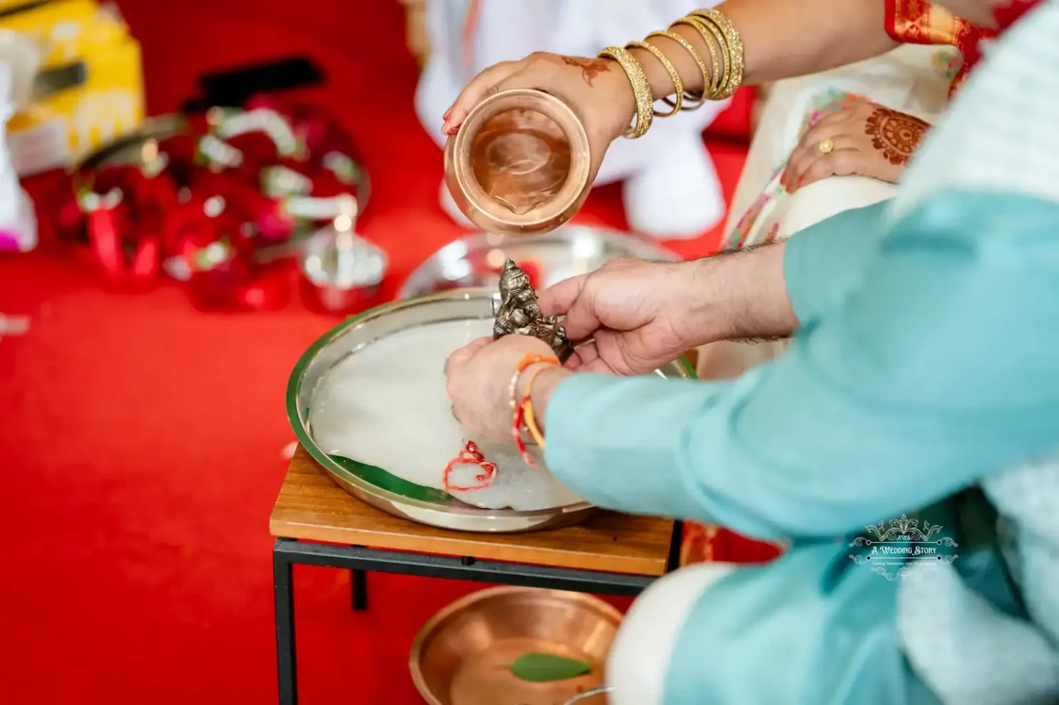 Close-up of hands performing a cultural water ritual in a wedding, with water poured from a copper vessel over a deity statue placed on a tray.