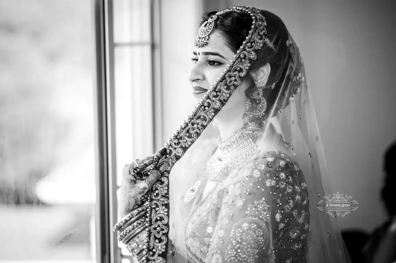 Black and white portrait of an Indian bride holding her veil, gazing out the window, captured in Wellington by Wedding Photography.