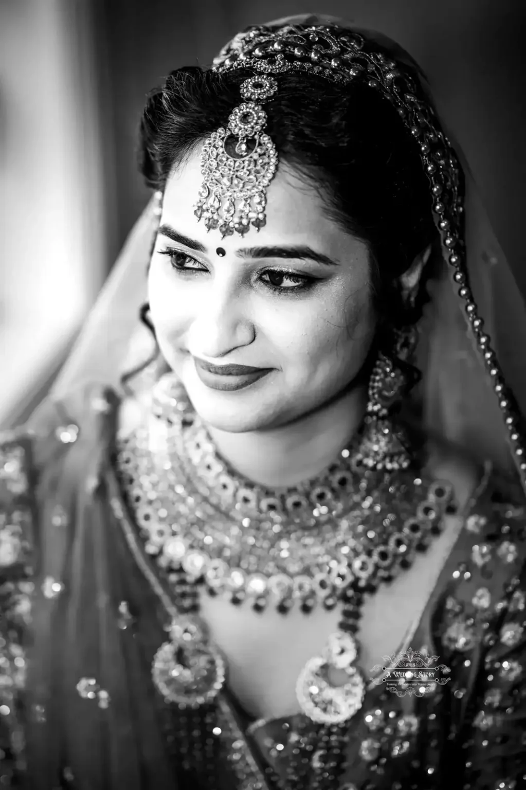 Black and white close-up portrait of a bride with traditional jewelry, smiling gracefully.