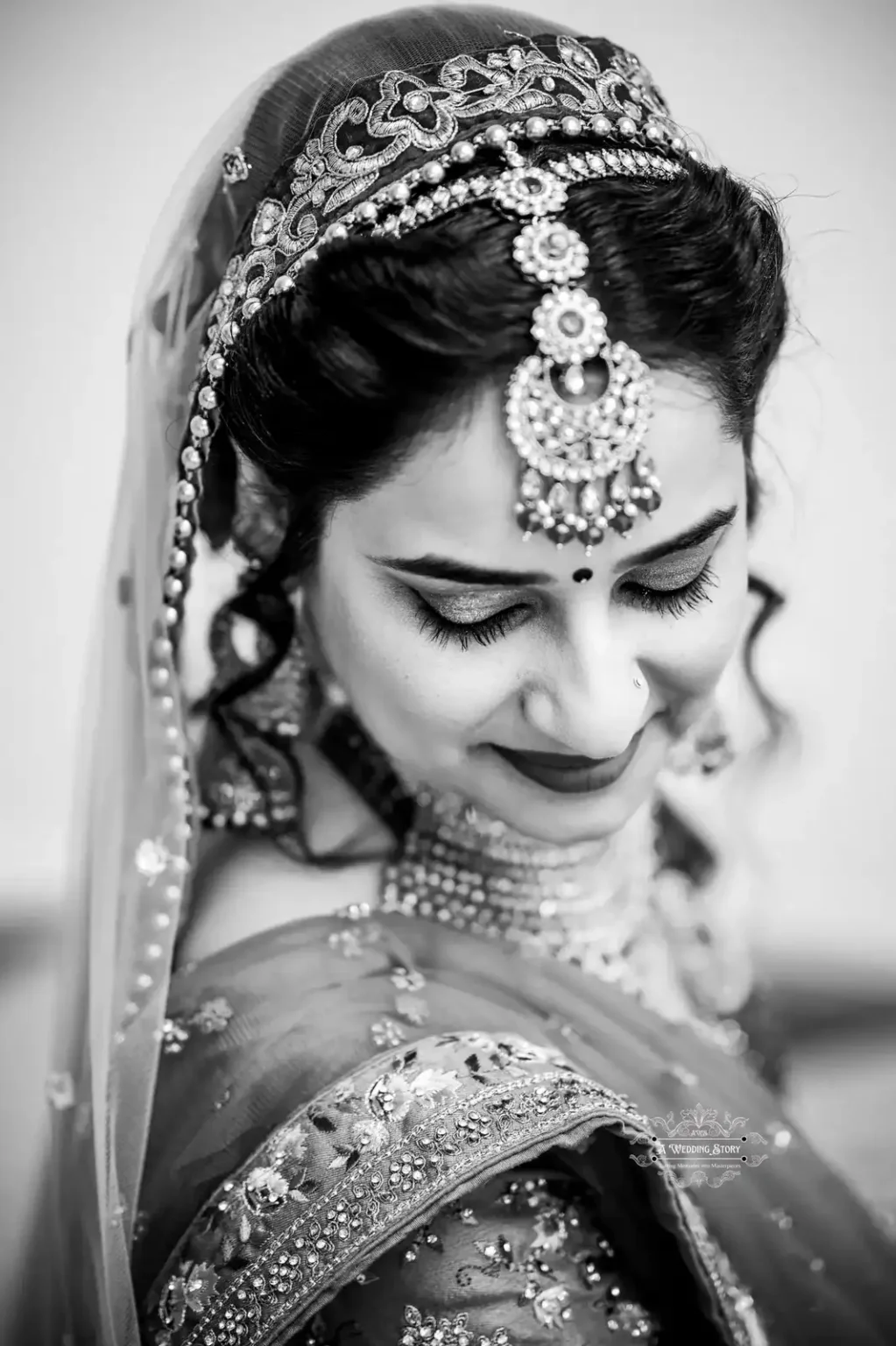 Black and white portrait of an Indian bride with traditional jewelry, looking down gracefully, captured by Wedding Photography in Wellington.