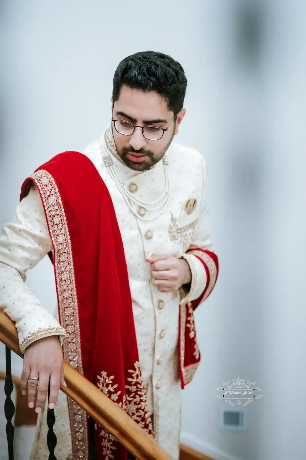 Indian groom in traditional wedding attire with a red shawl, leaning on a railing, captured in Wellington by Wedding Photography.