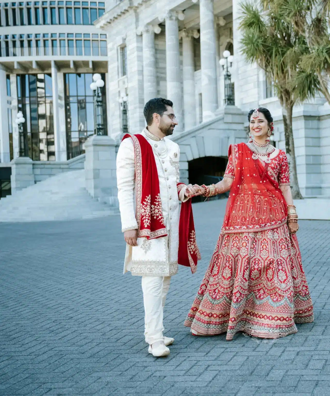 Bride and groom in traditional wedding attire posing outside a historic building in Wellington, New Zealand.