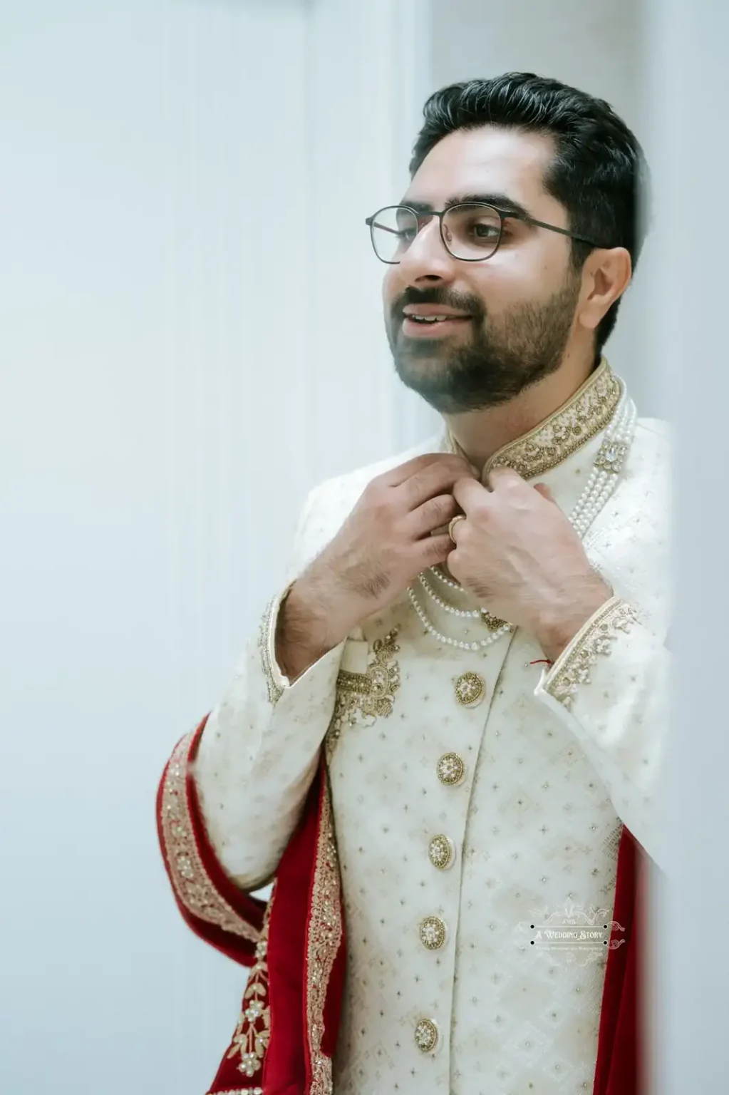 Indian groom adjusting his necklace, dressed in traditional attire with a red shawl, captured in Wellington by Wedding Photography.