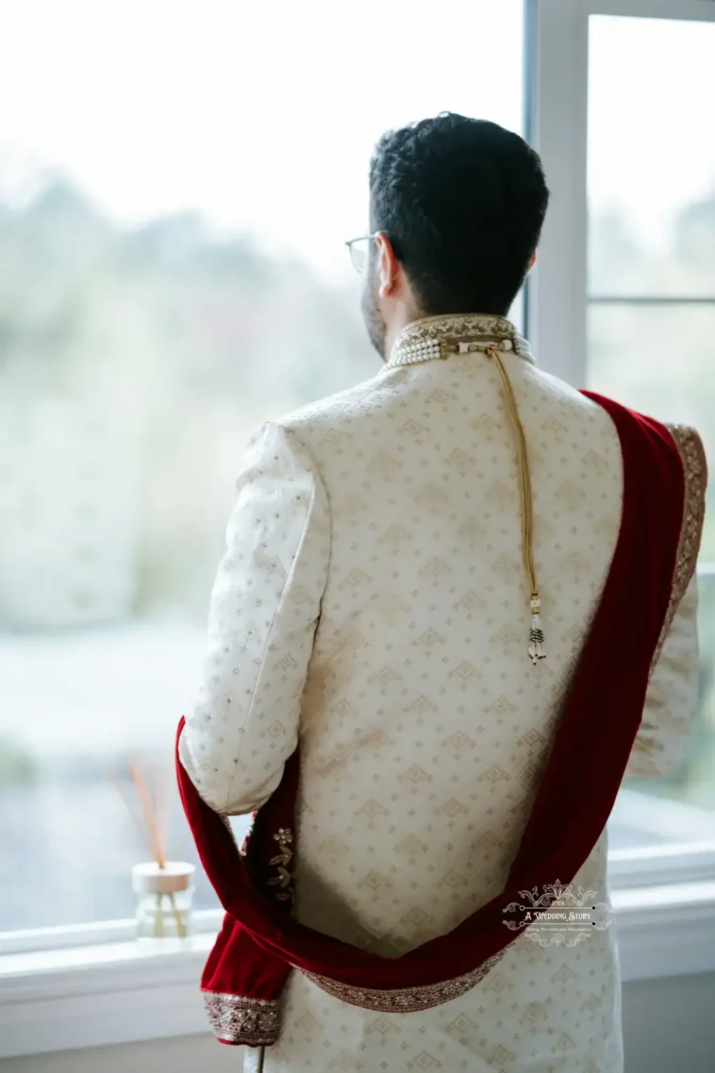 Indian groom in traditional wedding attire looking out the window before the wedding ceremony, captured in Wellington by Wedding Photography.