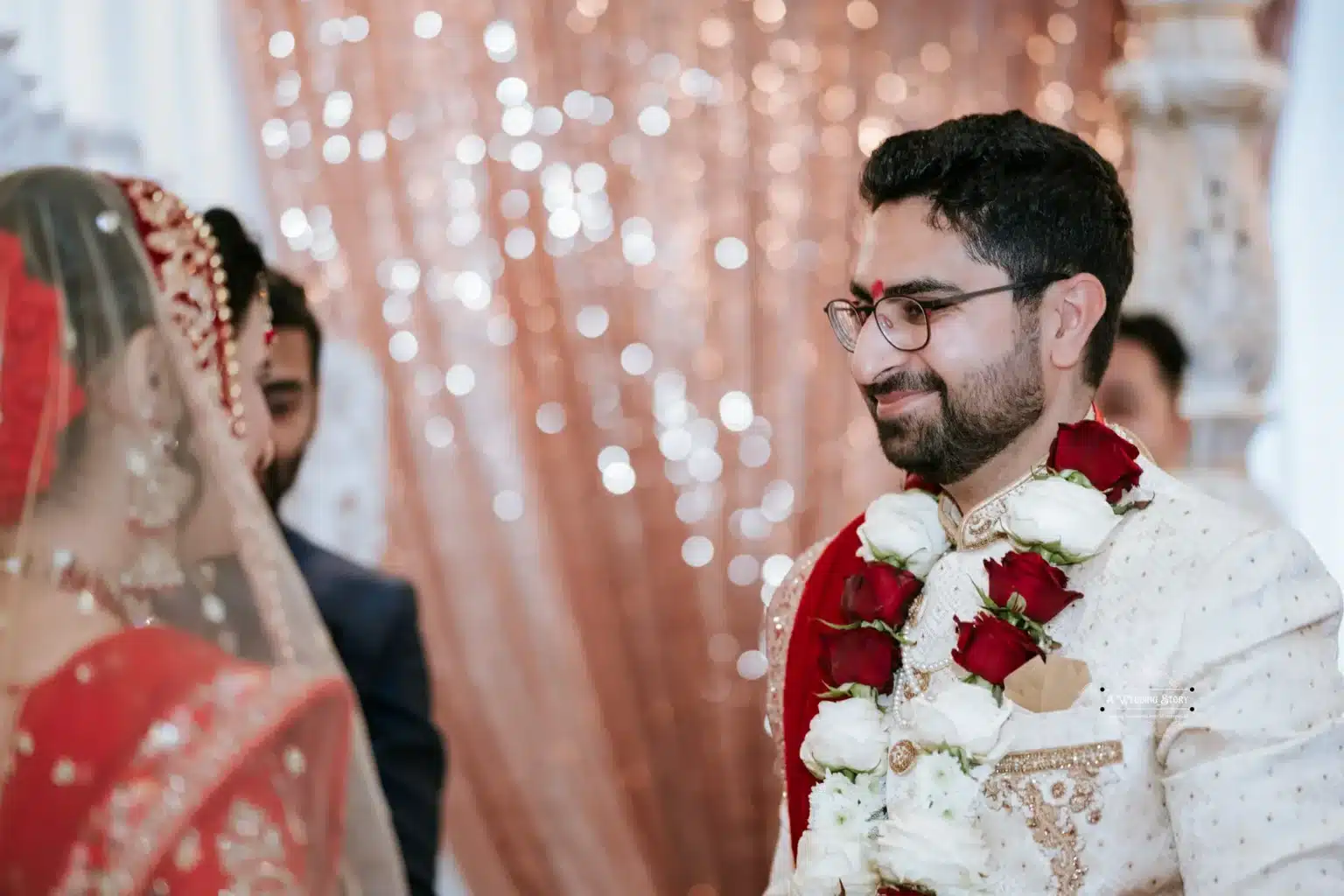 Groom in traditional attire, smiling at the bride during the wedding ceremony with floral garlands.