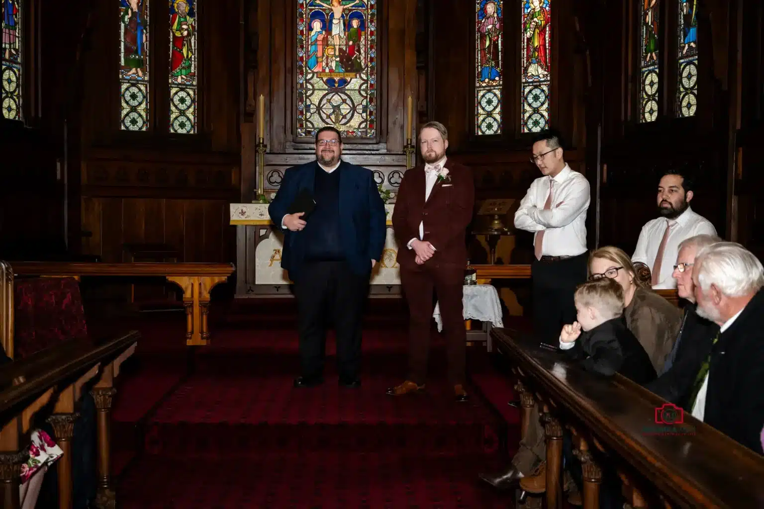 Groom and guests waiting in a dimly lit church with stained glass windows